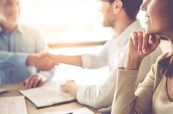 seated colleagues shaking hands at a conference table